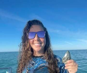 A diver holding a large fossil megalodon shark tooth in front of blue ocean and sky