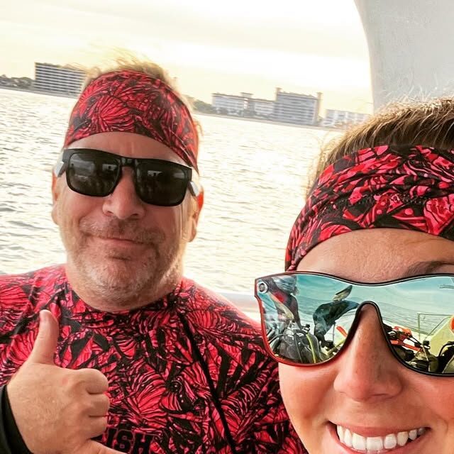 Two divers in matching shark-tooth patterned wetsuit tops smiling and giving a thumbs up on a boat offshore